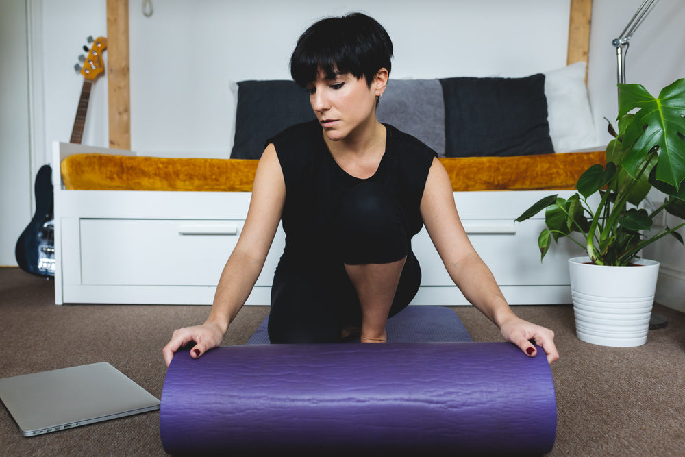 woman rolls purple yoga mat onto living room floor