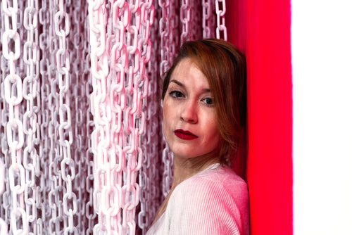 woman sandwiched between a red wall and a curtain of white chains