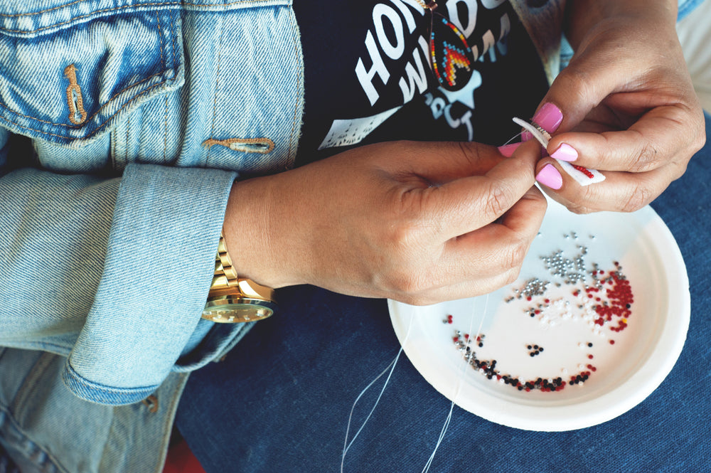 woman sewing with silver and red beads