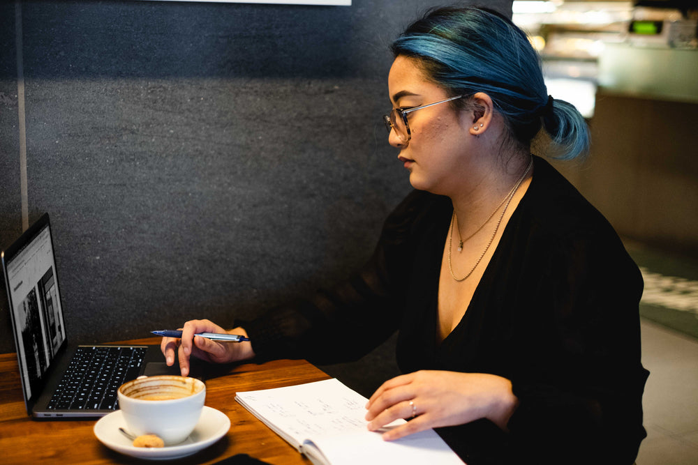 woman sits alone in a quiet cafe with a notebook and laptop