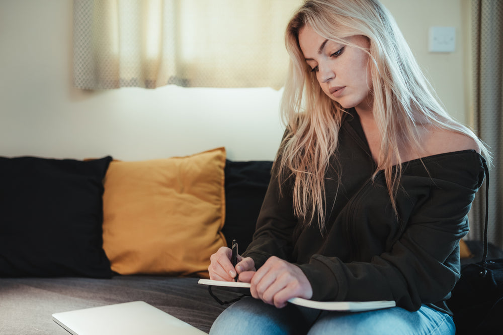 woman sits alone journalling in a black notebook