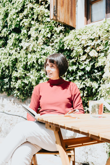 woman sits at a wooden table and holds a book