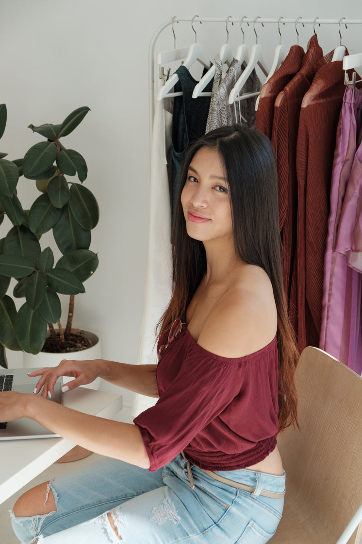 Woman Sits At Her Laptop With A Rack Of Clothes Behind Her