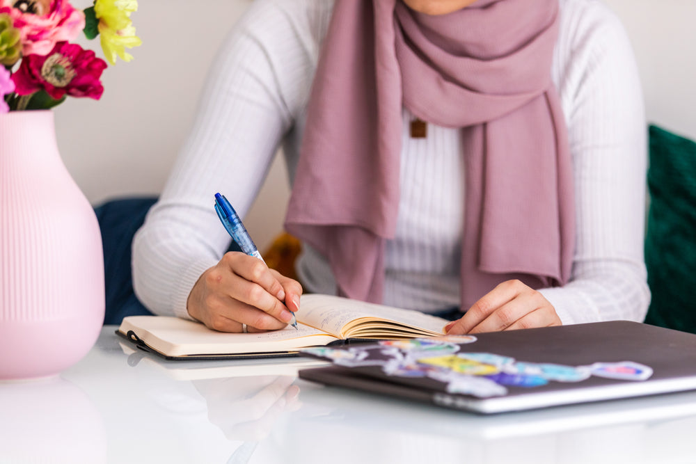 woman sits at table making notes in journal