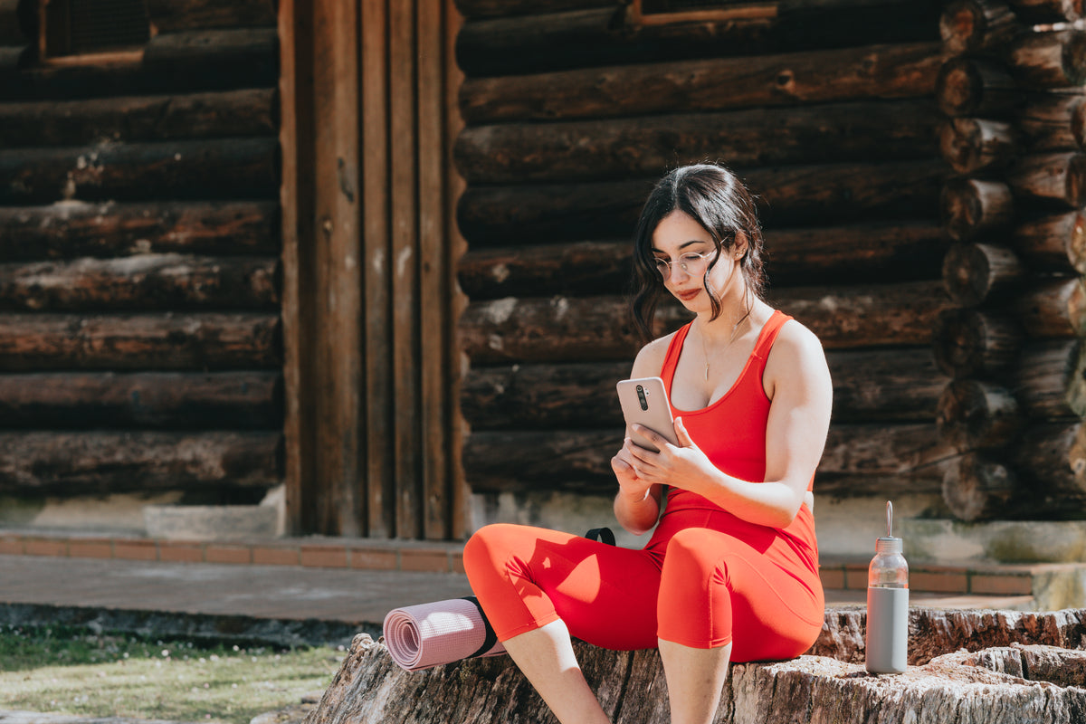 woman sits by a wood cabin and looks at her phone