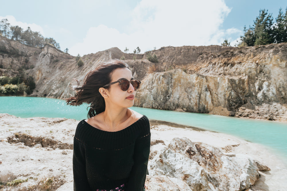 woman sits by rocks and aqua blue water