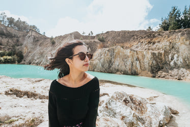 woman sits by rocks and aqua blue water