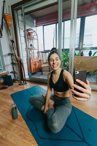 woman sits cross legged smiling at their cell phone