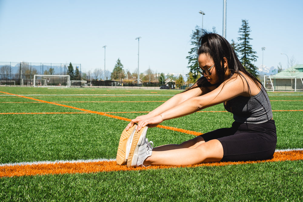 woman sits holds her toes in a stretch outdoors