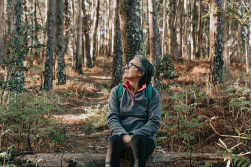 woman sits in a forest and looks up smiling
