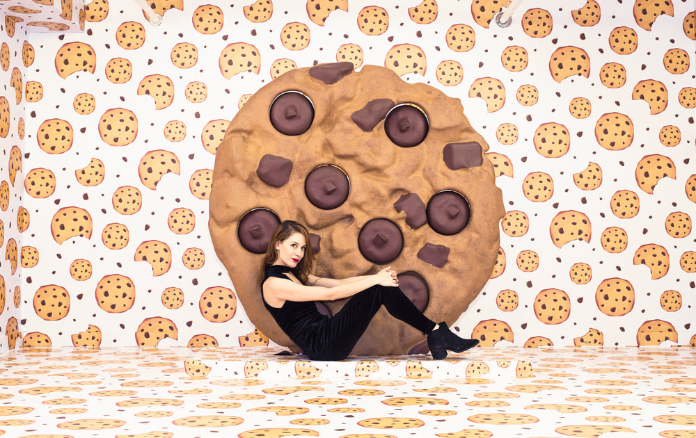 woman sits next to a giant cookie in a cookie-themed room