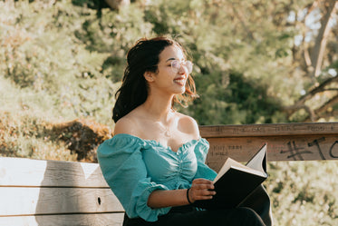 woman sits on a bench outdoors with a book smiling