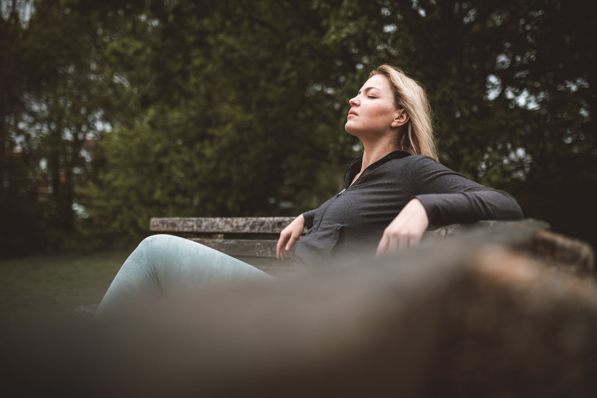 woman sits on a bench outdoors with eyes closed