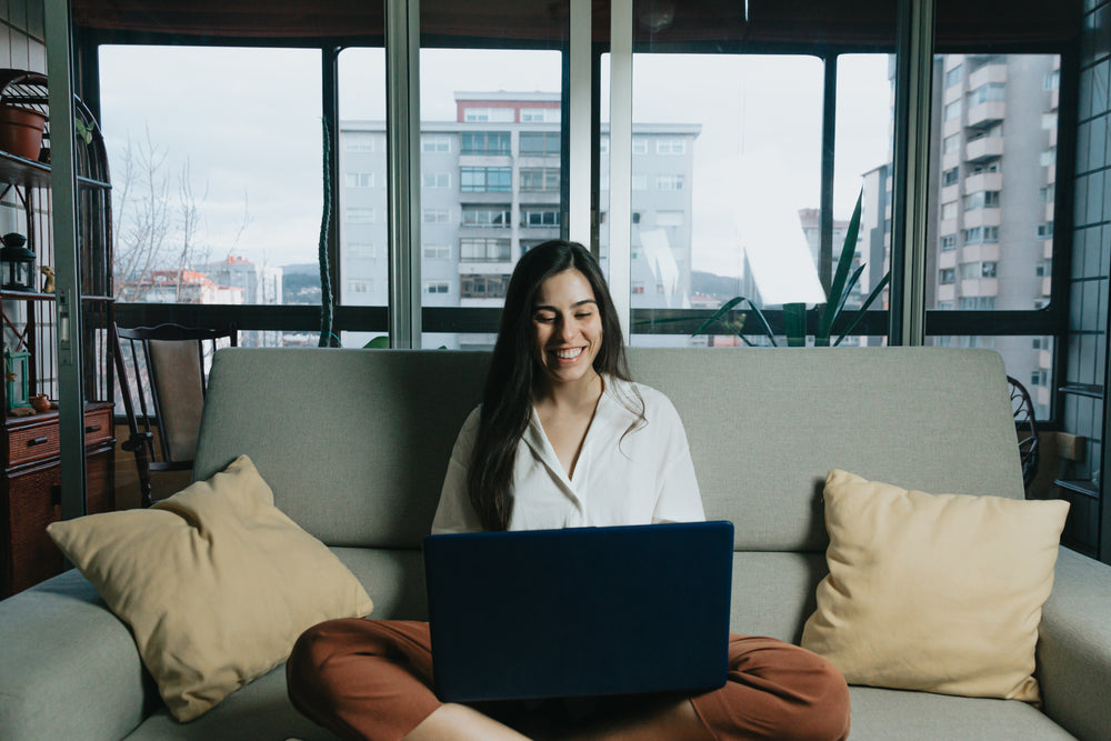 woman sits on a couch while looking at laptop