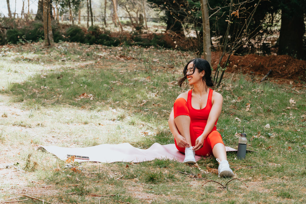 woman sits on a pink yoga mat on green grass