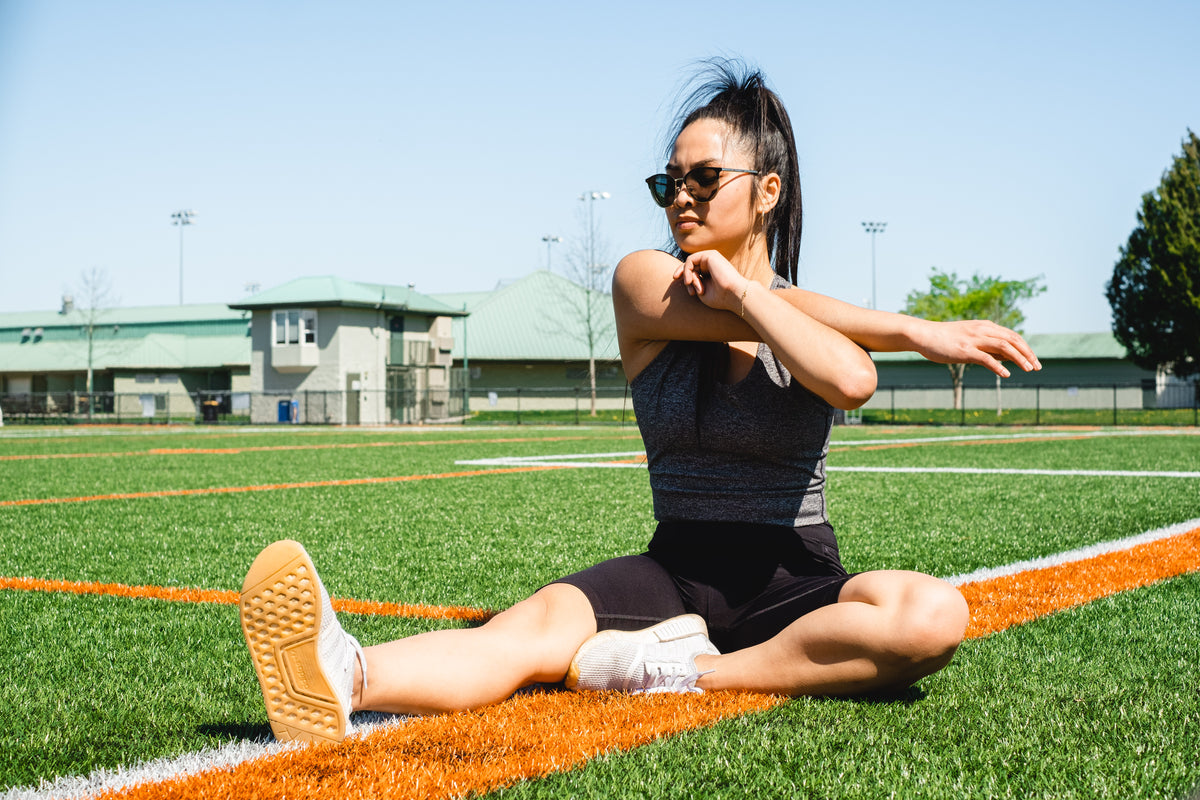 woman sits on a sports fields and stretches her arms