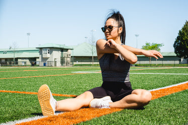 woman sits on a sports fields and stretches her arms