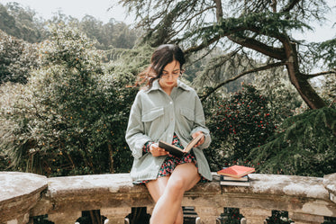 woman sits on a stone surface and reads a hardcover book