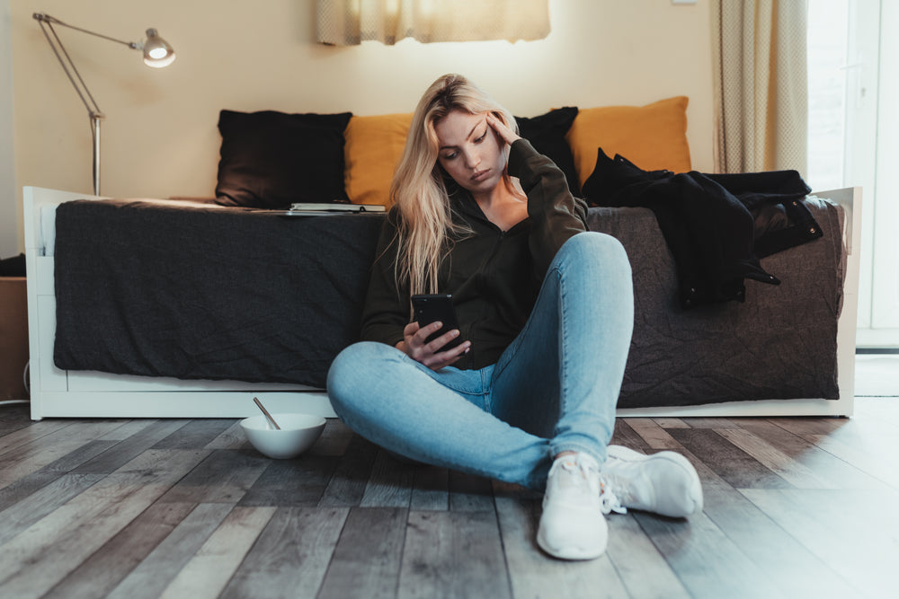 woman sits on floor and looks at her cell phone