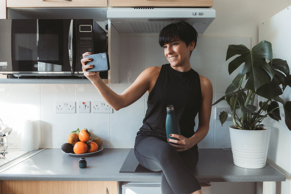 woman sits on her kitchen counter and takes selfie