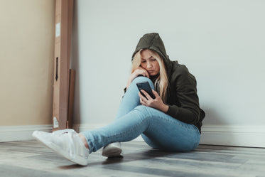 woman sits on the floor and looks at her cellphone