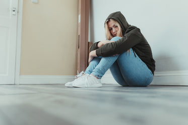 woman sits on the floor with her arms around her legs