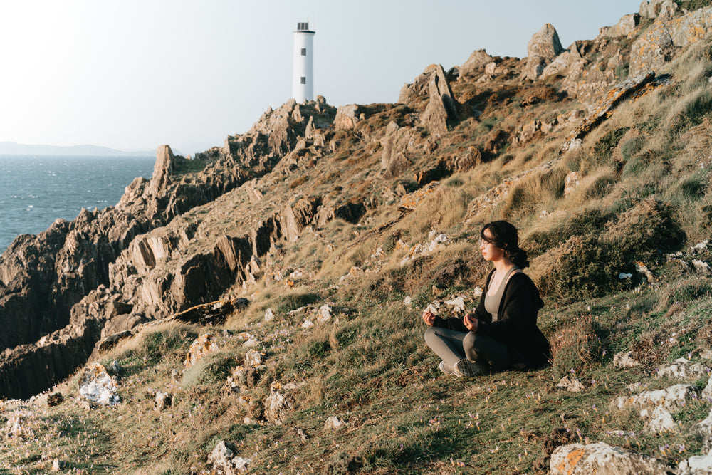 woman sits on the side of a hill above water