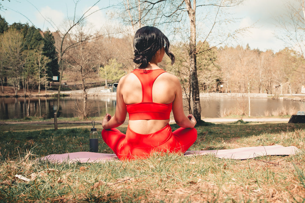 woman sits outdoors on a pink yoga mat