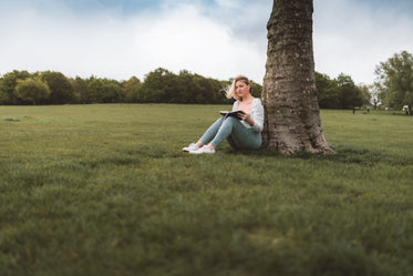 woman sits under a tree and reads a book in the breeze