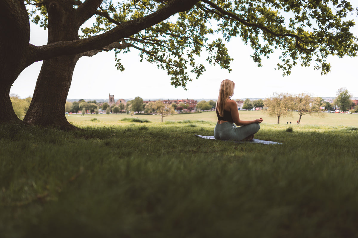 woman sits under large tree on a yoga mat
