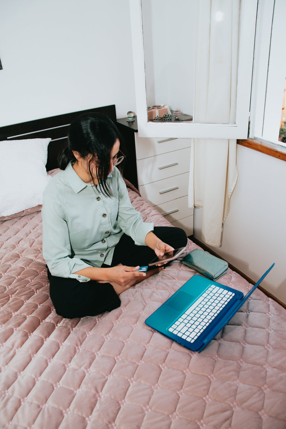 woman sitting on pink bed with her laptop and pphone