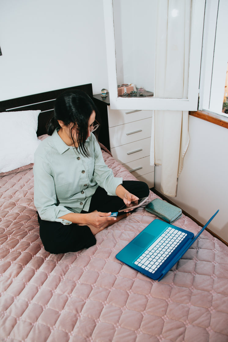 Woman Sitting On Pink Bed With Her Laptop And Pphone