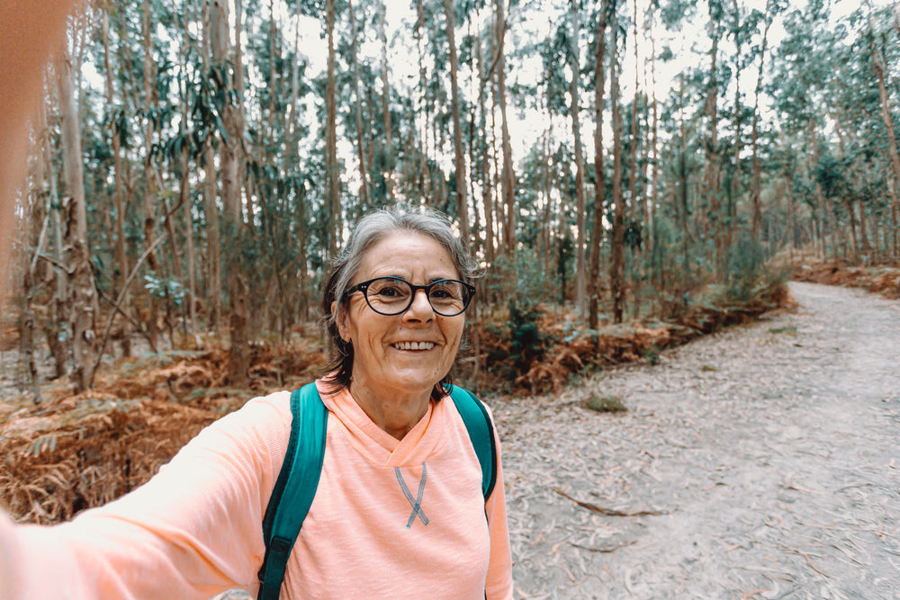 woman smiles and takes a selfie while out on a hike