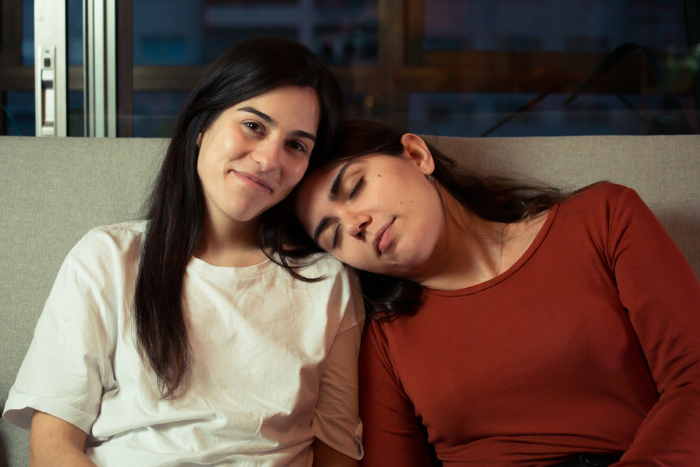 woman smiles as a woman sleeps on her shoulder