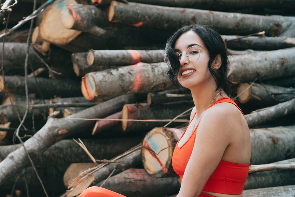 woman smiles at the camera while standing wood stack