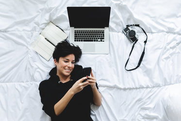 woman smiles laying on a bed looking at her phone