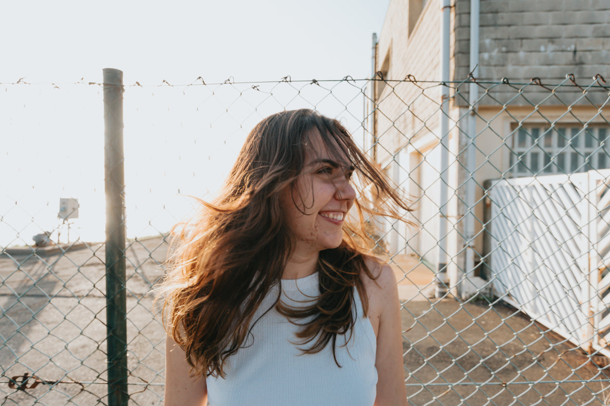woman smiles wide standing in front of a fence