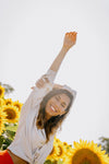 woman smiles with one arm up to the sun in a sunflower field