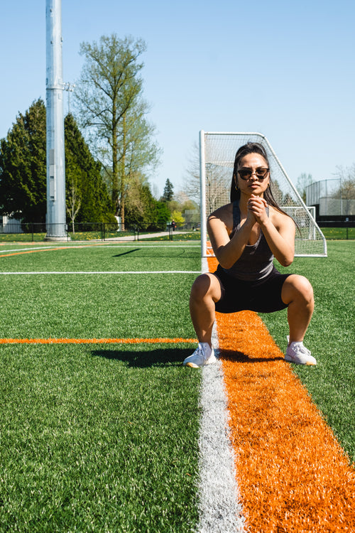woman squats in workout gear on a grassy field