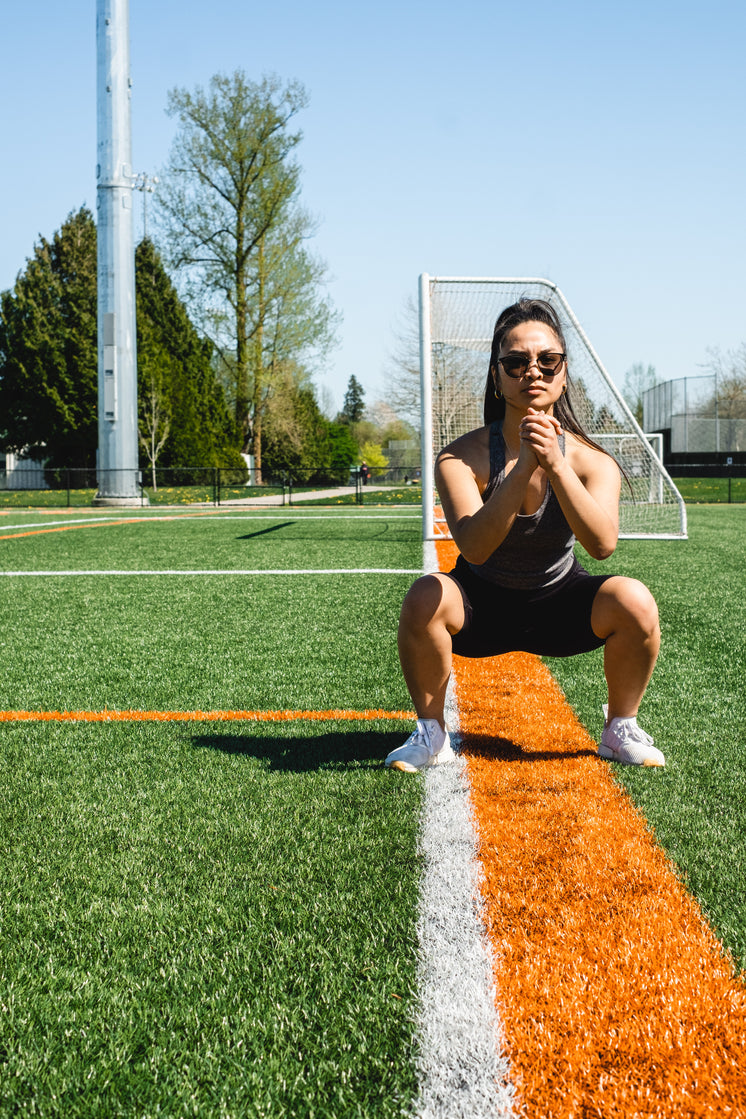 Woman Squats In Workout Gear On A Grassy Field