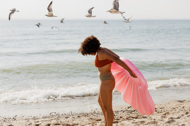 woman standing on beach holding pink inflatable shell toy