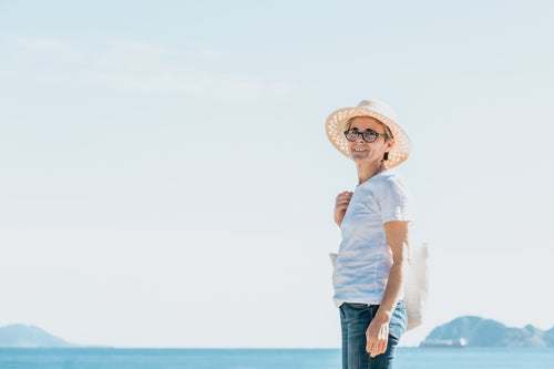 woman stands by open water and a straw hat