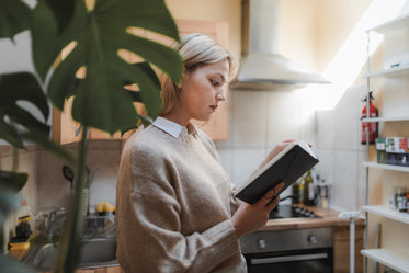 woman stands in her kitchen with a book in hand