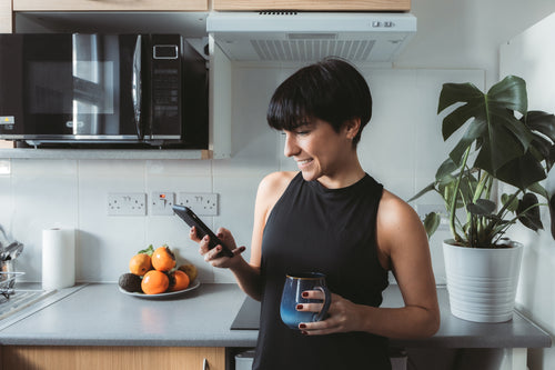 一个女人站在厨房里，一边用手机一边微笑