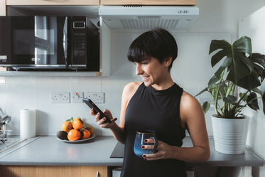 woman stands in the kitchen and smiles while using cell phone