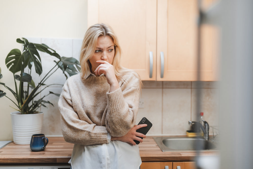 woman stands in the kitchen with her hand close to her face