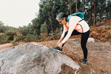 woman stops on a hike to tie their shoe