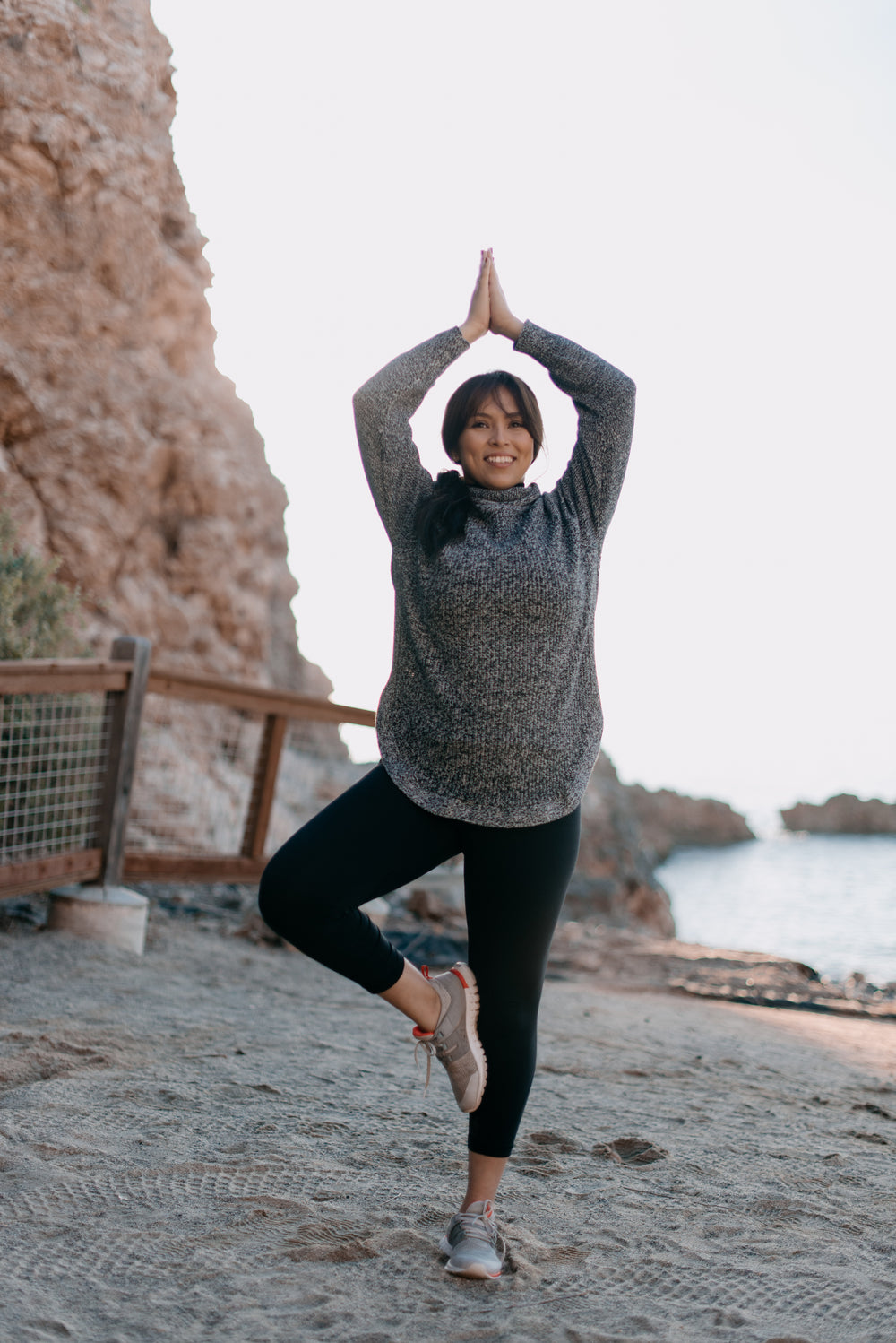 woman strikes a tree pose on the beach