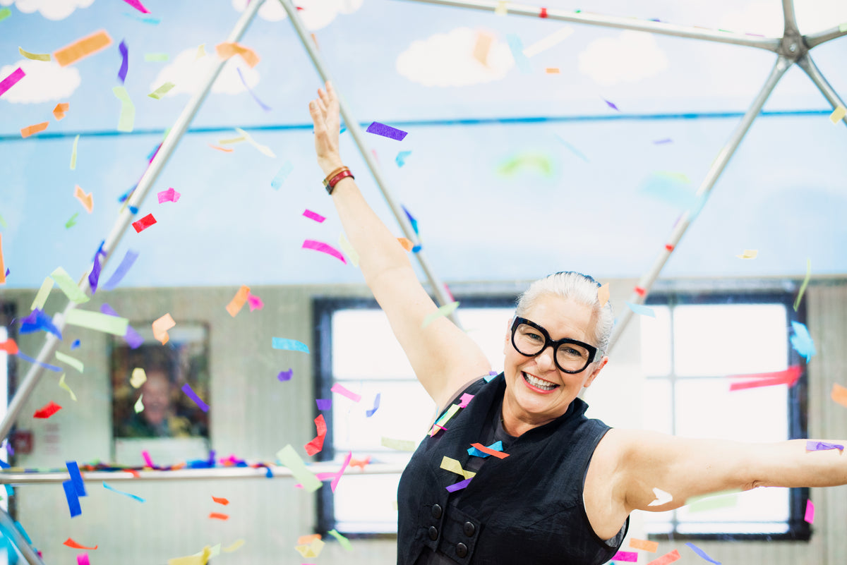 woman throws arms in air as rainbow confetti falls around her