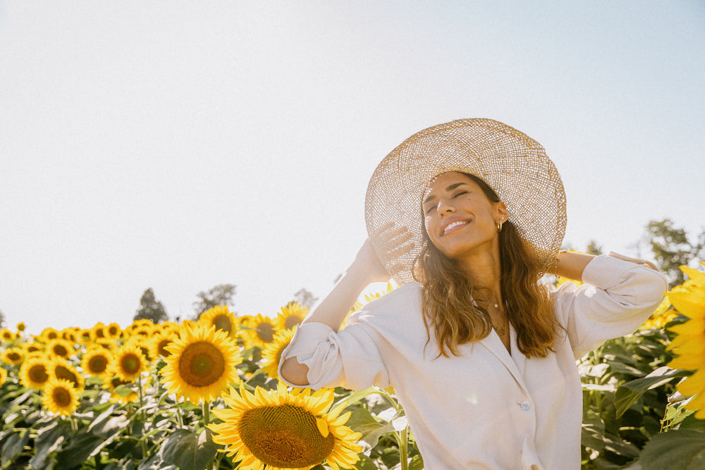 woman tilts her head up towards the sun holding onto hat